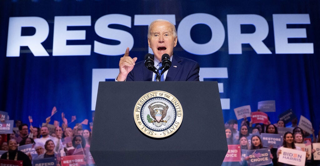 President Joe Biden, in a blue suit and tie, speaks into a microphone at a pro-abortion rally.