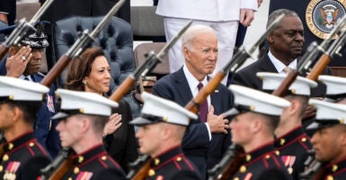 Kamala Harris, Joe Biden, and Lloyd Austin in suits stand behind members of the military in uniform