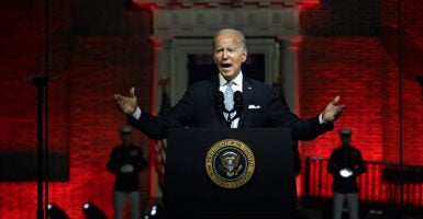 President Joe Biden gestures in a black suit in front of Philadelphia's Independence Hall behind the presidential seal