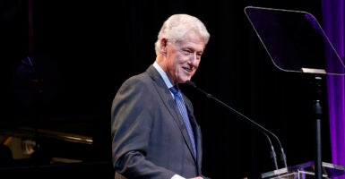 Bill Clinton in a grey suit speaks behind a teleprompter