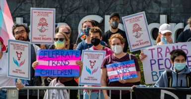 Protesters wearing masks hold signs reading "Celebrate trans children" and "trans kids belong"