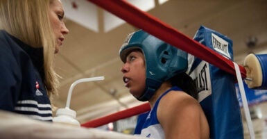 Cary Williams stands with one of her female boxing athletes in the ring while holding a water bottle.