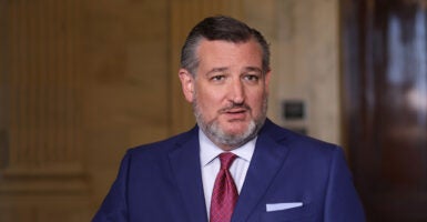 Sen Ted Cruz standing in a blue suit and red tie while speaking to members of the press.