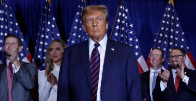 Donald Trump looks intently in a blue suit with an American flag pin.