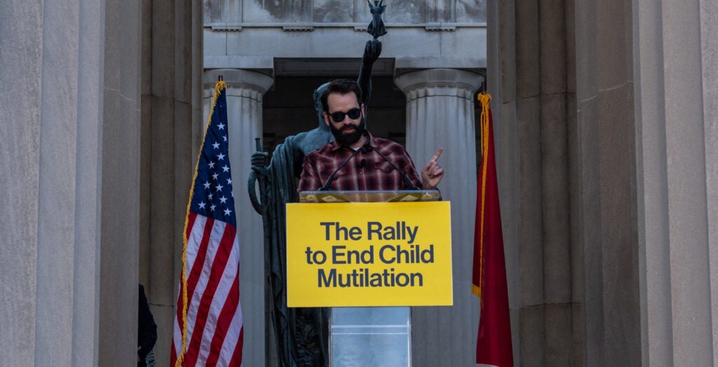 Conservative commentator Matt Walsh speaks in front of an American flag and behind a sign reading "The Rally to End Child Mutilation"