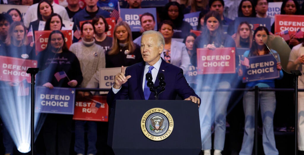 President Joe Biden speaks at a rally at a podium in a suit with a crowd behind him