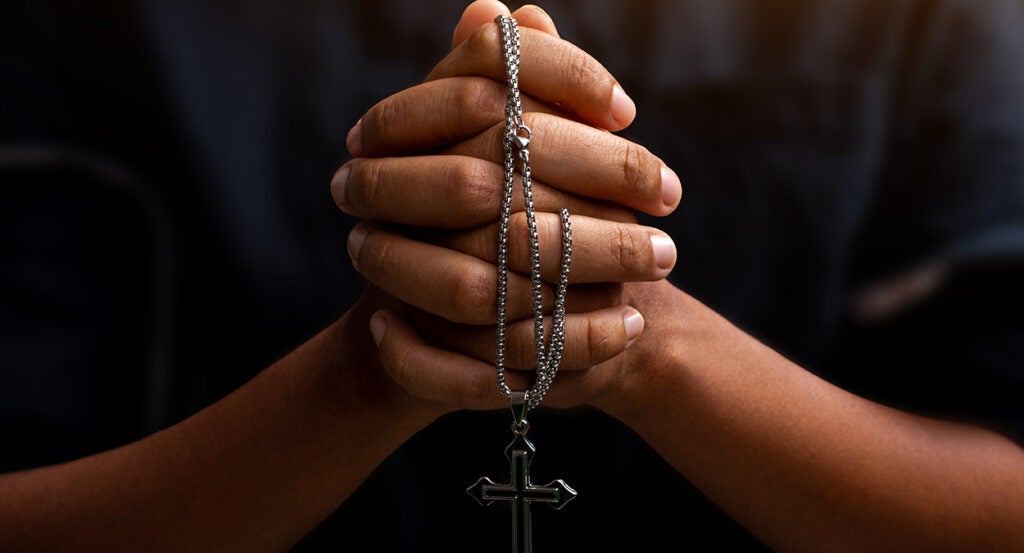 A black person prays with a crucifix