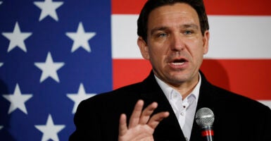 Ron DeSantis in a black suit stands in front of an American flag