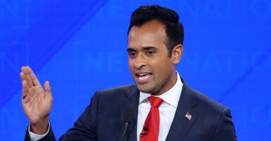 Vivek Ramaswamy gestures in a black suit with a red tie and an American flag pin