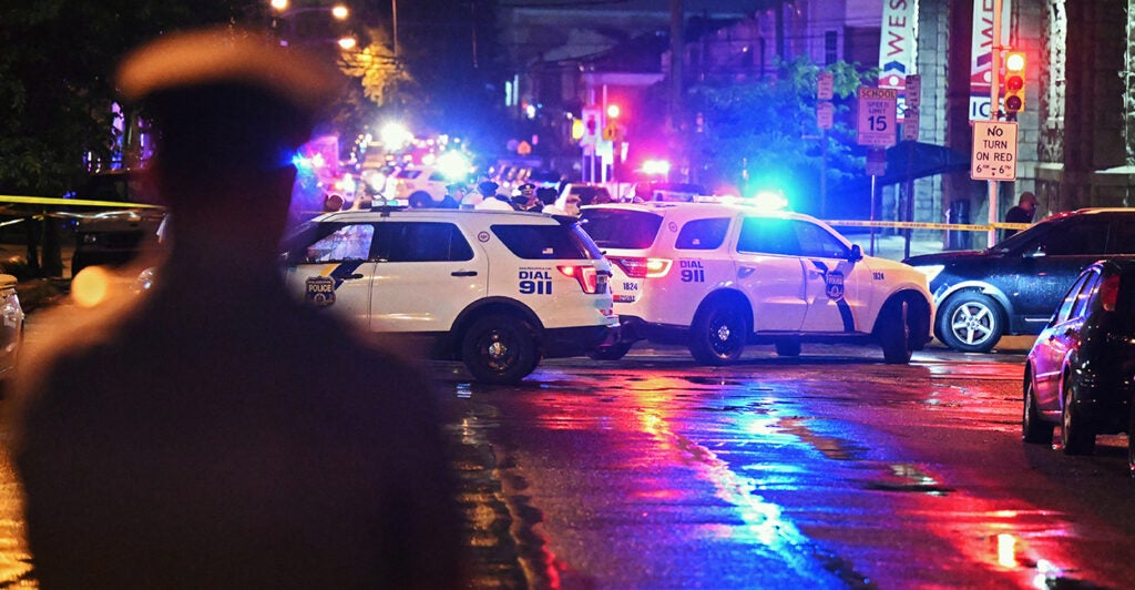 2 police cars with lights flashing blocking the road at night in Philadelphia with a police officer looking on