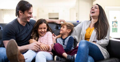 Mom, Dad, and a young son and daughter sitting on a couch at home laughing