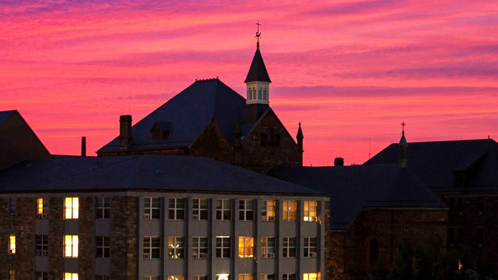 Castle-like building outlines pink sunset with some lights on in windows.