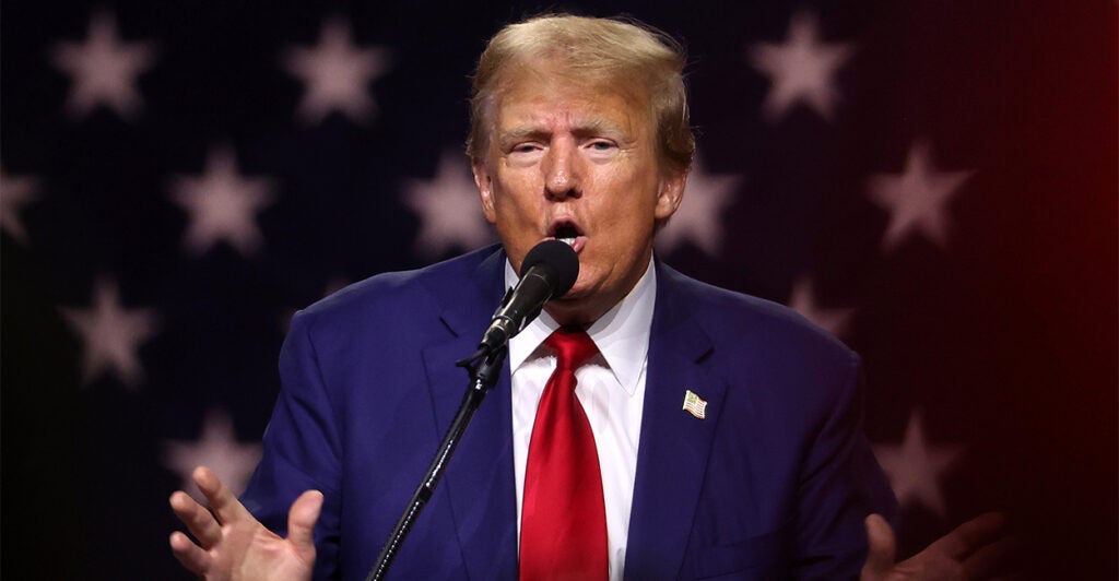 Former President Trump on stage at a Campaign Rally wearing a blue suit and red tie