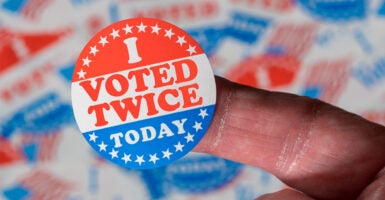 Finger with a voting sticker that says, "I voted twice today"