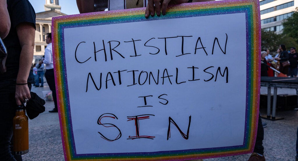 A sign with a rainbow frame reading "Christian Nationalism Is Sin."