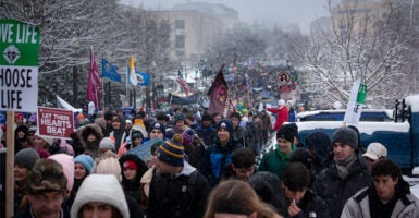 Large crowd in winter weather garb from the March for Life 2024 hold signs and flags.