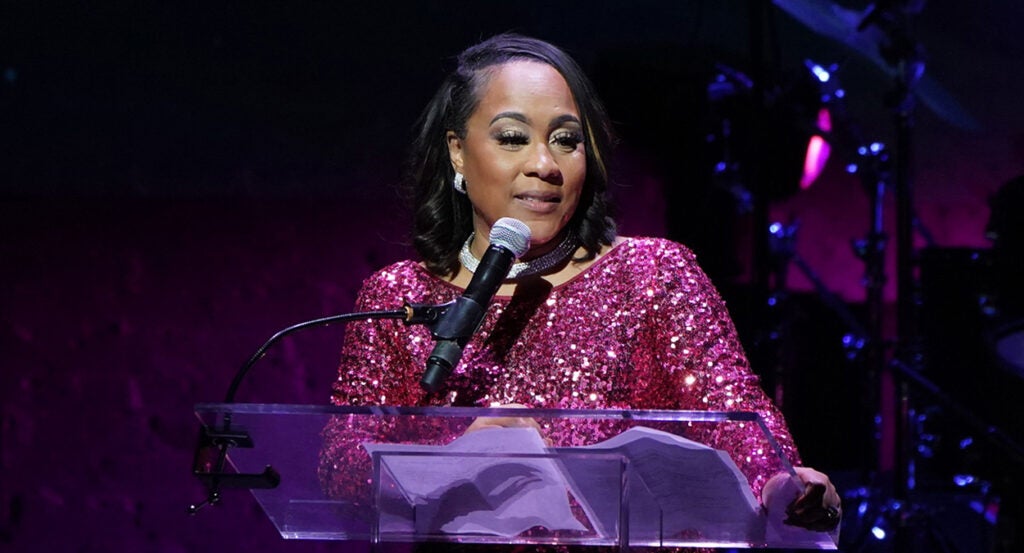 Fani Willis in a purple-y pink sparkly dress at The Root in front of a microphone