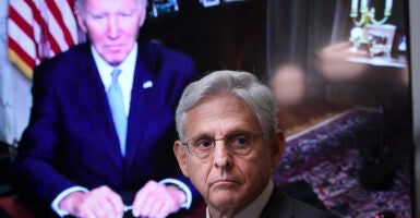 Attorney General Merrick Garland in a suit in front of a screen showing President Joe Biden in a blue suit.