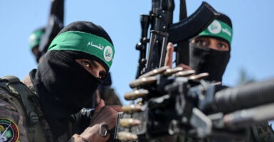 Two Hamas fighters in military regalia fire a machine gun