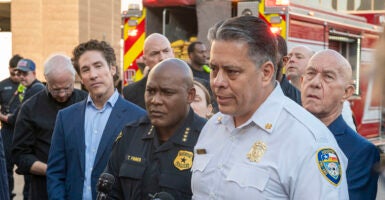 Joel Osteen in a blue suit listens as Fire Department Chief Samuel Pena and Mayor John Whitmire speak at a press conference