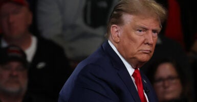 Former President Donald Trump looks to his side while on stage at a town hall. He is wearing a dark blue suit and red tie.