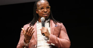 Ibram X. Kendi sits speaking into a microphone wearing a salmon blazer.