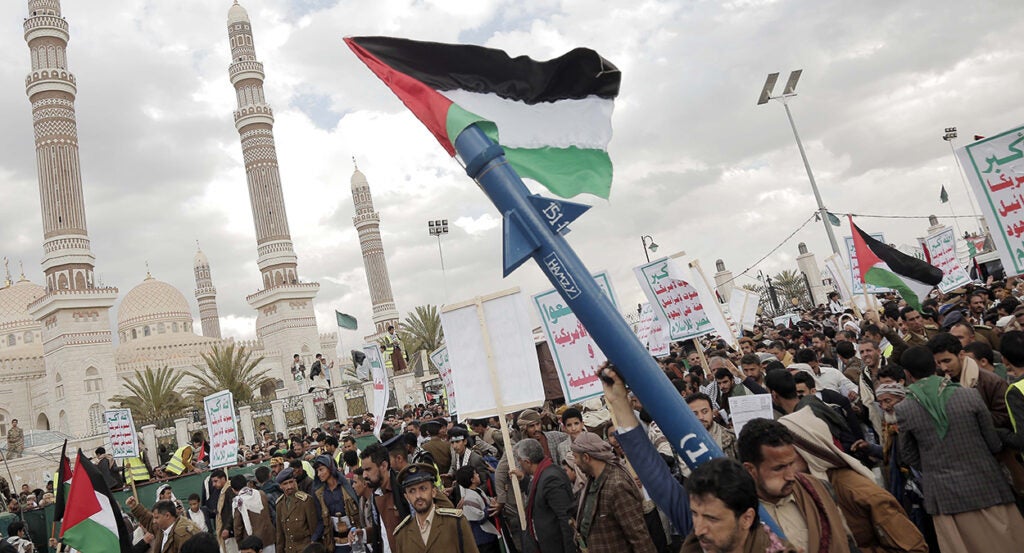 Houthi supporters protest in Yemen's capital, Sanaa, with one man holding a rocket and a Palestinian flag.