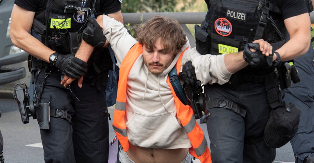 Two police officers carry a male demonstrator off the roadway