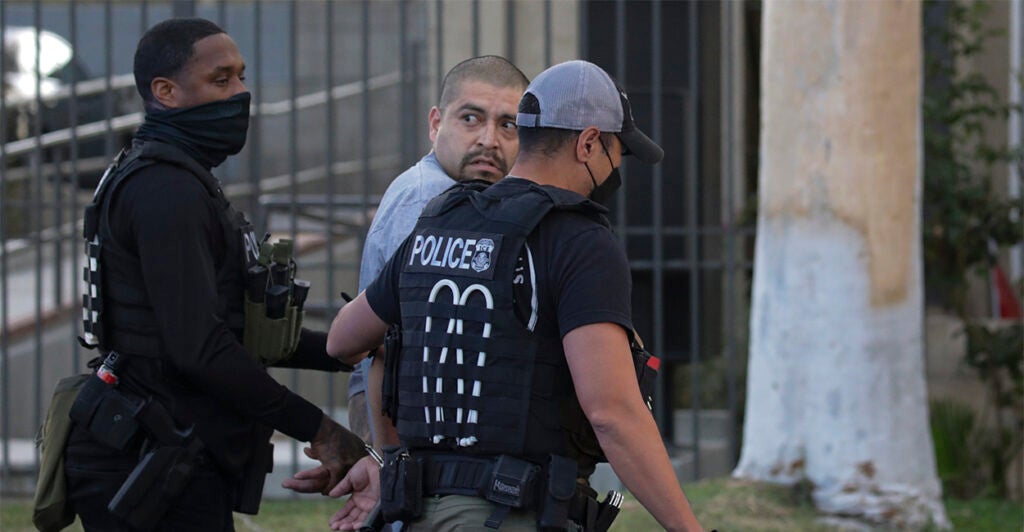 Two police officers walk an illegal immigrant gang member away in handcuffs