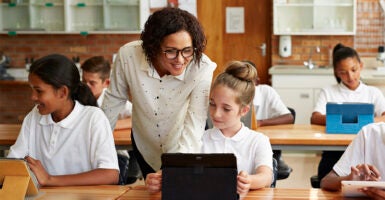 Young, female school teacher helping private school students in uniforms in class