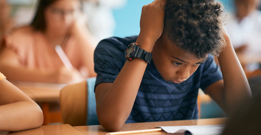 Black elementary student worried while reading exam paper during a class at school.