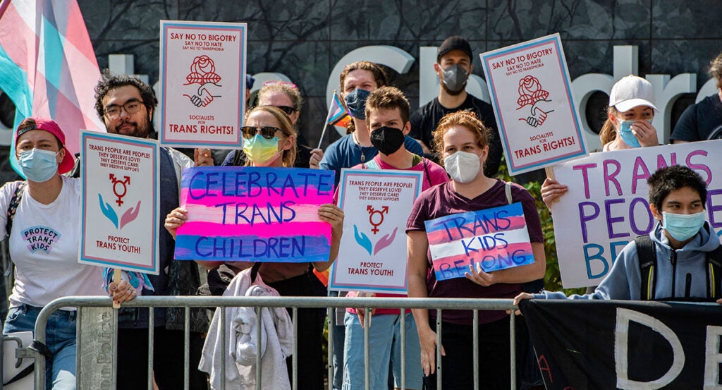 Protesters wearing face masks hold signs reading "Celebrate trans children," and "trans kids belong."