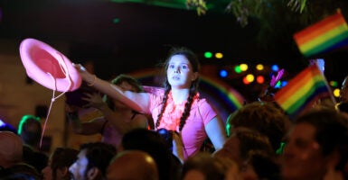 A young girl dressed in a pink shirt, holding a pink cowgirl hat, looks off into the distance at a gay pride event.