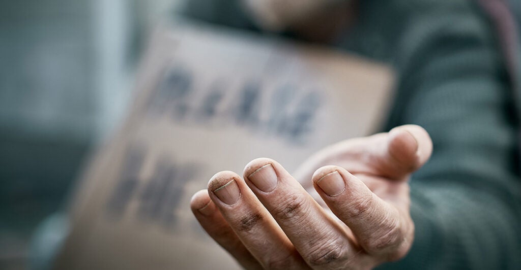 A man holds out his hand and a cardboard sign can be seen in the background.