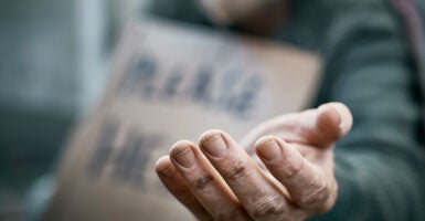 A man holds out his hand and a cardboard sign can be seen in the background.