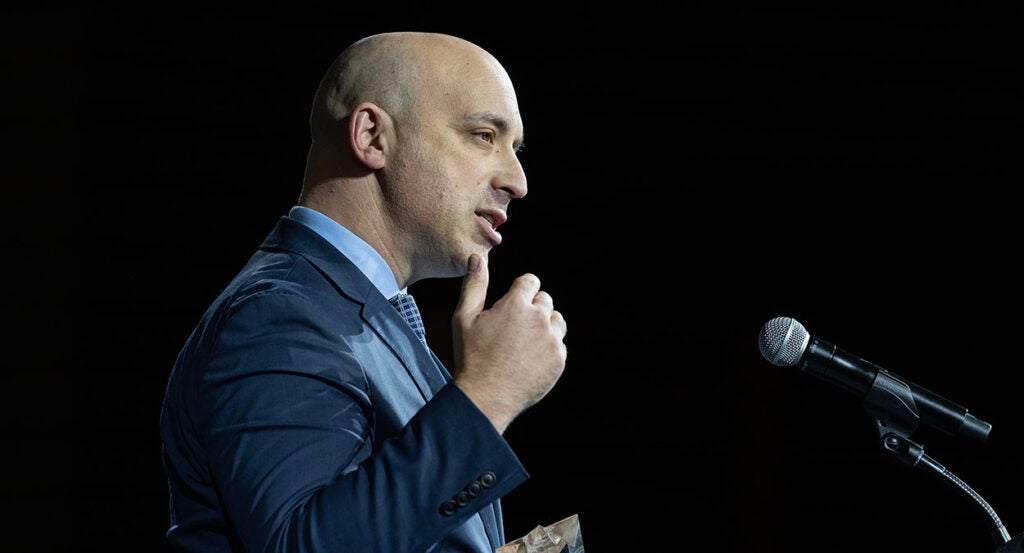 Jonathan Greenblatt in a blue suit gestures in front of a microphone