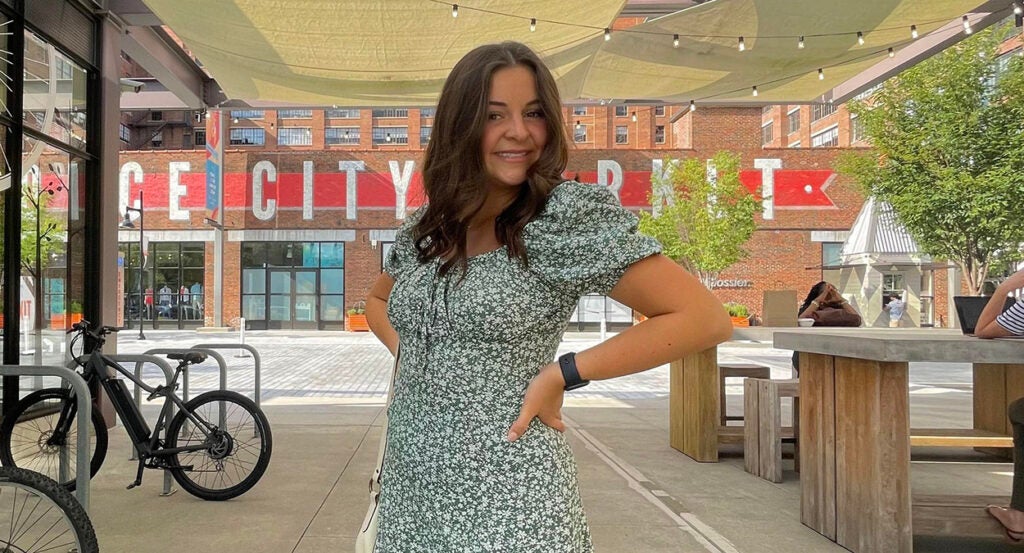 Laken Riley, a college coed, poses in front of a city market in a flower blouse.