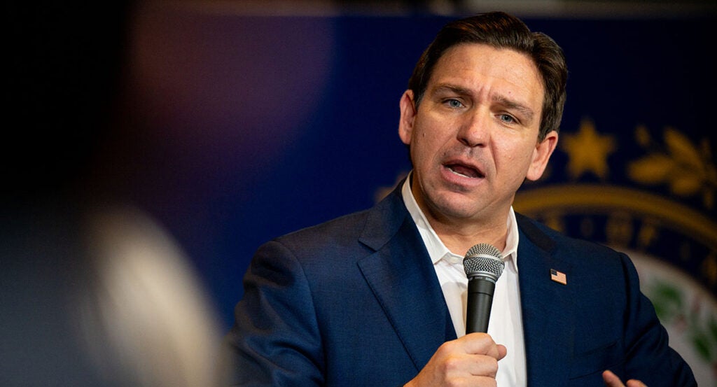 Ron DeSantis in a blue suit holds a microphone