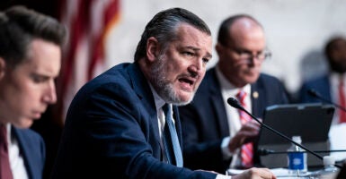 Sen. Ted Cruz, in a blue suit, pounds his fist on the table and speaks out