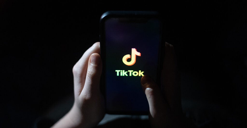 Children's hands hold a phone with the TikTok logo displayed.