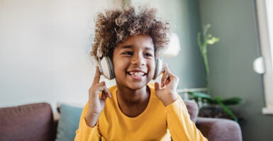 A smiling child sits on a chair, wearing headphones.