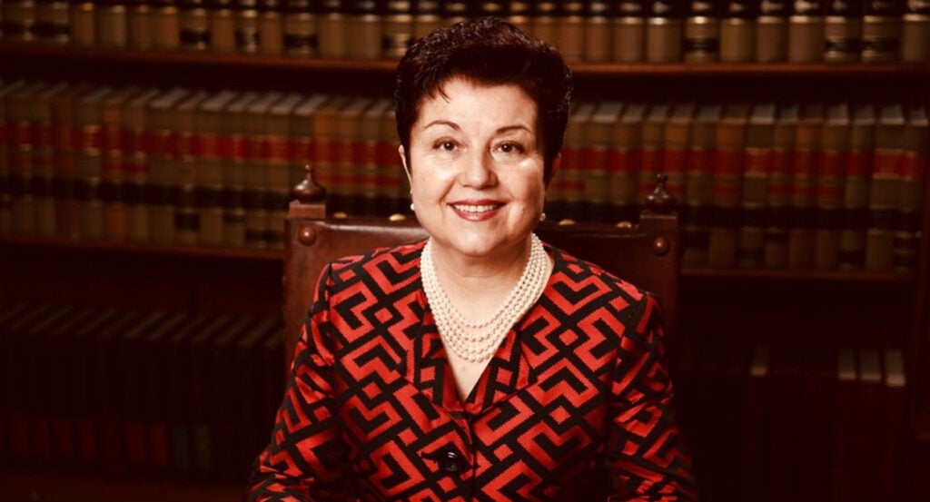 Virginia Prodan sits in front of bookshelves wearing a blouse and pearl necklace.