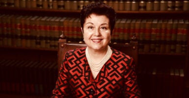 Virginia Prodan sits in front of bookshelves wearing a blouse and pearl necklace.