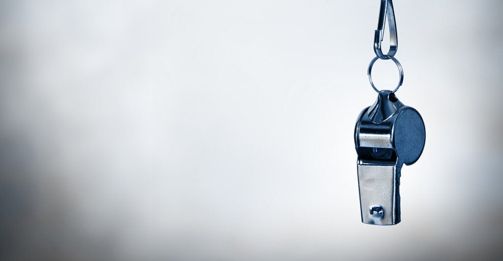 A silver whistle hands in front of a gray wall.