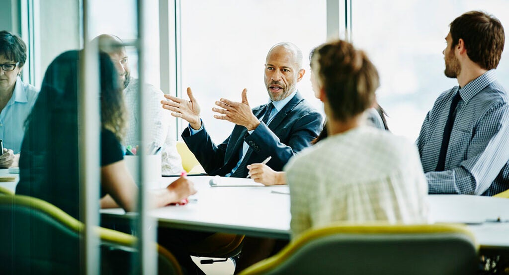 Corporate executive speaks in a suit to employees in dress clothes in a boardroom