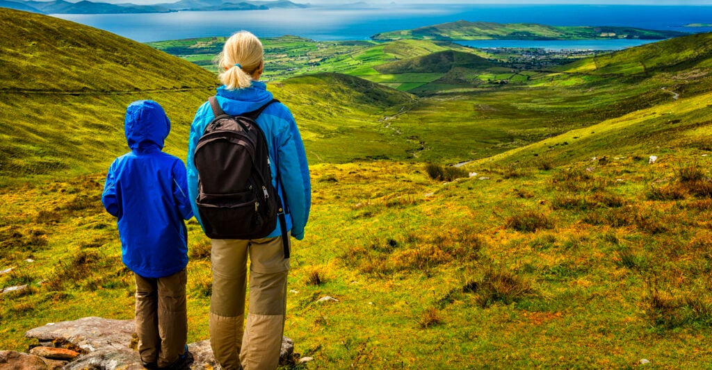 A blonde-haired woman and a young boy, both in blue-green jackets, stare out at the horizon in Ireland.