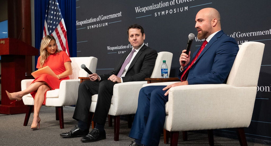 Kara Frederick in a red dress, Benjamin Weingarten in a black suit, and Michael Benz in a blue suit