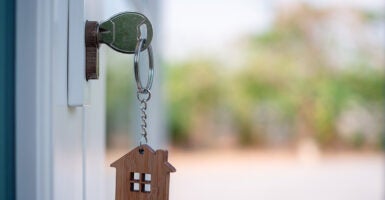 A key with a small wood house key chain hands from a white door.