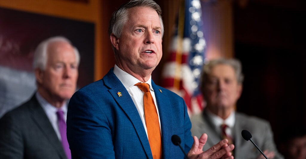 Sen Roger Marshall speaks at a podium in a blue suit and orange tie.