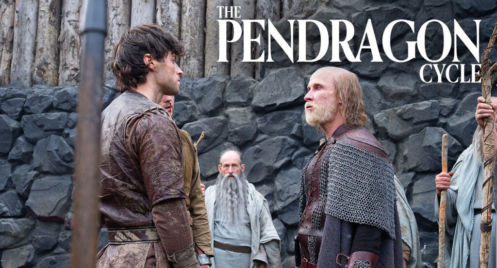 An elderly man with a beard and long hair beneath a bald spot stands in chain mail and armor confronting a young man with black hair in front of a rock wall. Text reading "The Pendragon Cycle" rests above their heads.